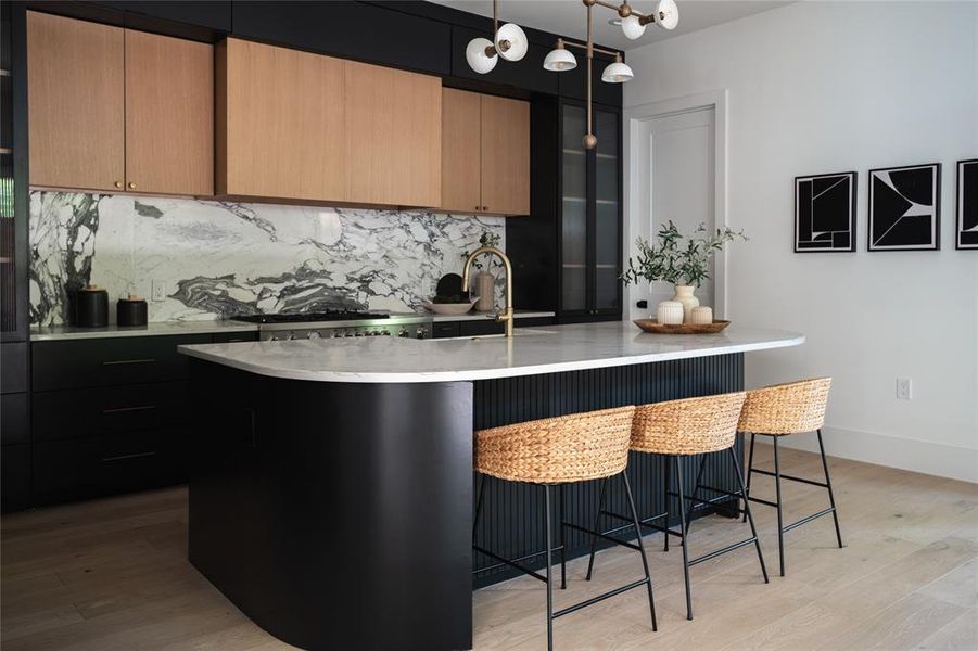 Kitchen featuring a kitchen breakfast bar, light hardwood / wood-style flooring, tasteful backsplash, an island with sink, and pendant lighting