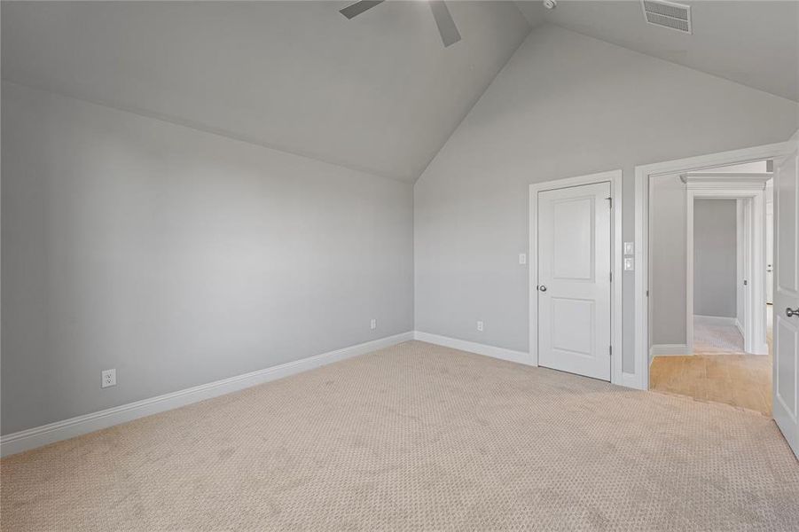 Carpeted empty room with high vaulted ceiling and ceiling fan