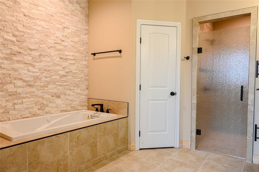 Primary bath has deep soaking tub and lovely accent stone wall.