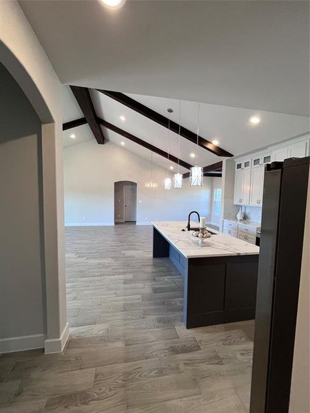 Kitchen with light hardwood / wood-style floors, lofted ceiling with beams, white cabinets, decorative light fixtures, and a center island with sink