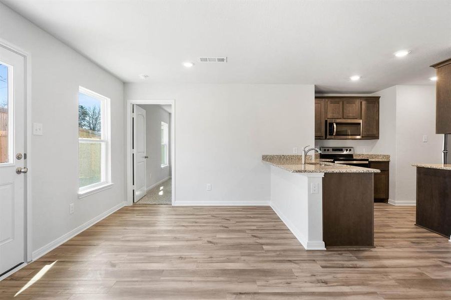 Kitchen featuring appliances with stainless steel finishes, light stone counters, light hardwood / wood-style floors, sink, and kitchen peninsula