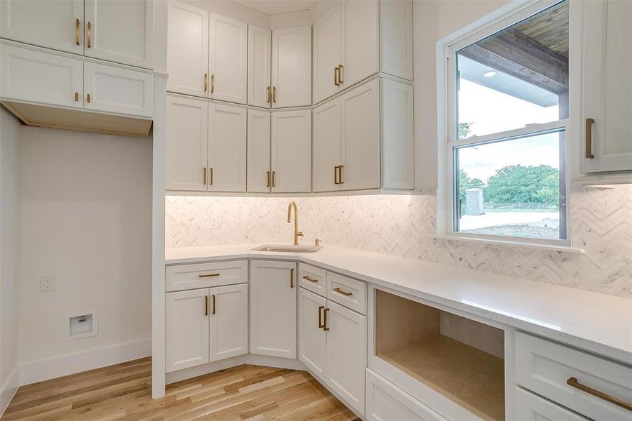 Kitchen featuring decorative backsplash, sink, light wood-type flooring, and white cabinetry