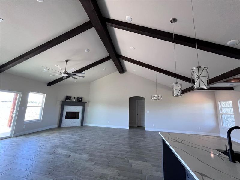 Kitchen with ceiling fan, vaulted ceiling with beams, wood-type flooring, decorative light fixtures, and a fireplace