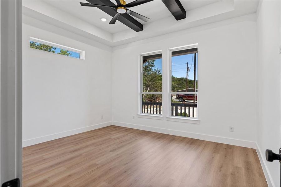 Empty room with ceiling fan, light hardwood / wood-style flooring, and a tray ceiling