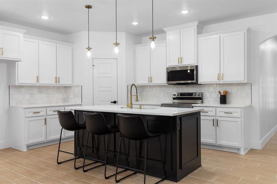 Kitchen with white cabinetry, decorative light fixtures, decorative backsplash, a center island with sink, and appliances with stainless steel finishes