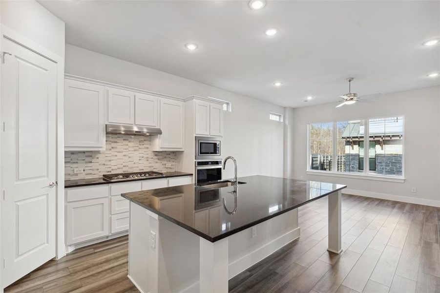 Kitchen with a center island with sink, hardwood / wood-style flooring, tasteful backsplash, white cabinetry, and appliances with stainless steel finishes