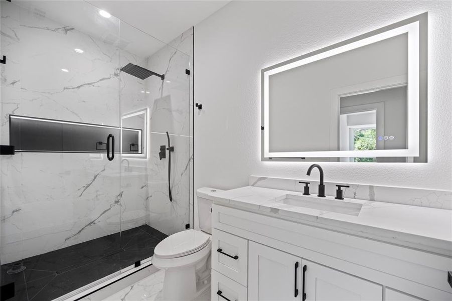 Bathroom featuring a shower with shower door, vanity, tile patterned flooring, and toilet