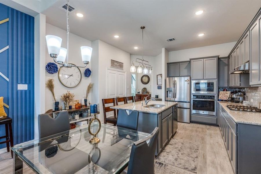 Kitchen with light stone counters, hanging light fixtures, sink, light hardwood / wood-style flooring, and stainless steel appliances