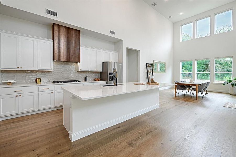 Kitchen featuring stainless steel appliances, decorative backsplash, white cabinets, light wood-type flooring, and a kitchen island with sink