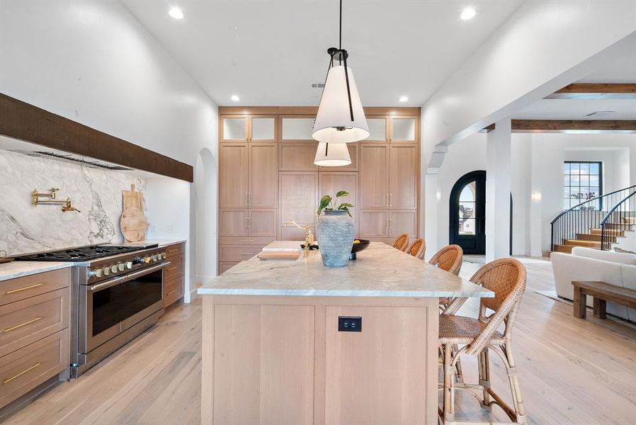 Kitchen featuring premium range, light wood-type flooring, tasteful backsplash, and a center island with sink