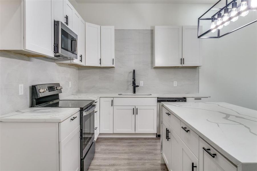 Kitchen featuring light hardwood / wood-style floors, backsplash, hanging light fixtures, white cabinetry, and appliances with stainless steel finishes
