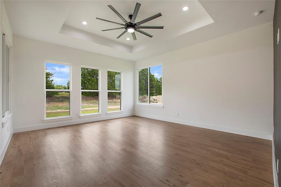 Empty room with ceiling fan, hardwood / wood-style floors, and a tray ceiling