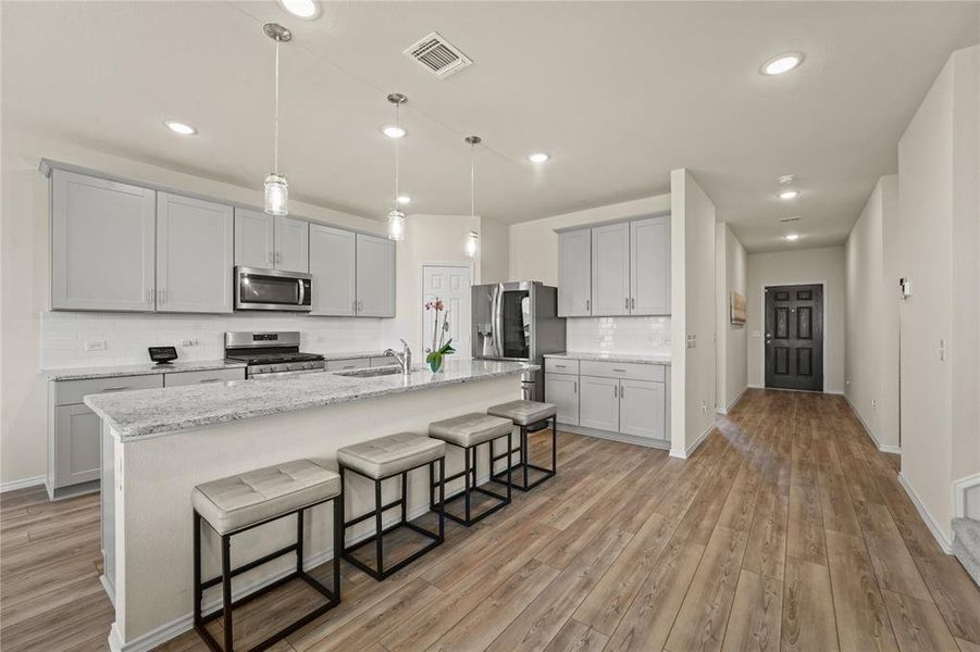 Kitchen with stainless steel appliances, decorative backsplash, light wood-type flooring, a breakfast bar, and a kitchen island with sink