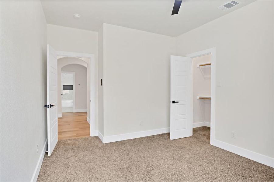 Unfurnished bedroom featuring a walk in closet, ceiling fan, light colored carpet, and a closet