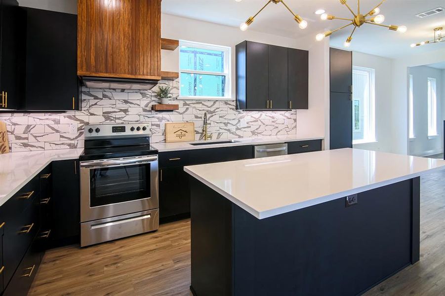 Kitchen with light hardwood / wood-style flooring, backsplash, stainless steel electric stove, and a kitchen island