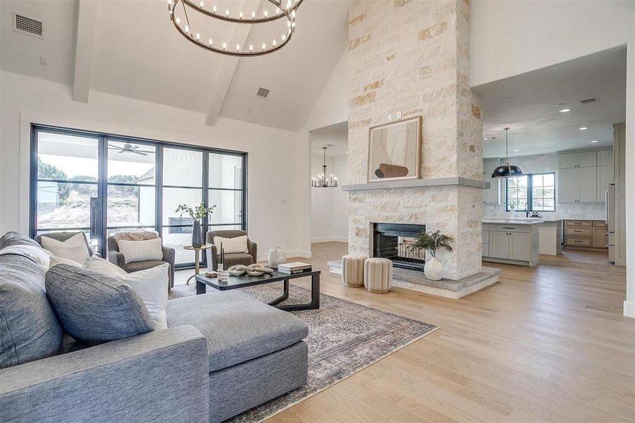 Living room with high vaulted ceiling, light wood-type flooring, a fireplace, beam ceiling, and a notable chandelier