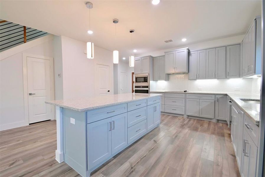 Kitchen with a center island, light hardwood / wood-style flooring, stainless steel appliances, and decorative light fixtures