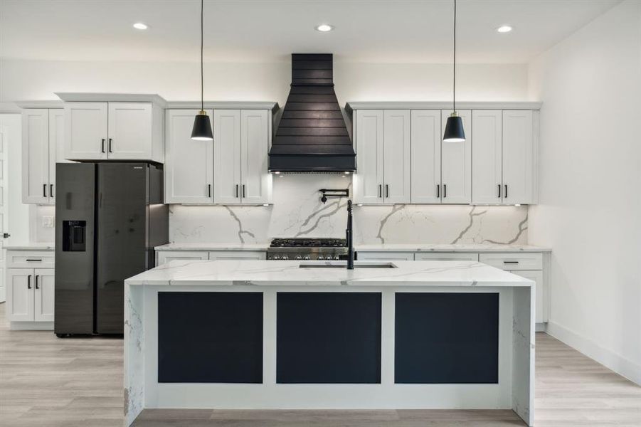 Kitchen featuring stainless steel fridge with ice dispenser, decorative light fixtures, white cabinets, and custom range hood