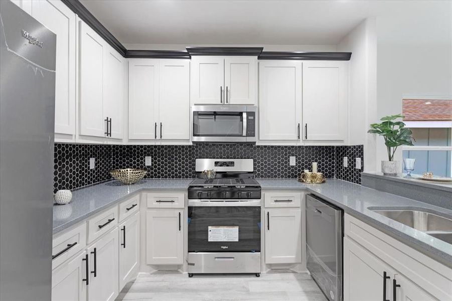 Kitchen with appliances with stainless steel finishes, light hardwood / wood-style floors, white cabinets, and backsplash