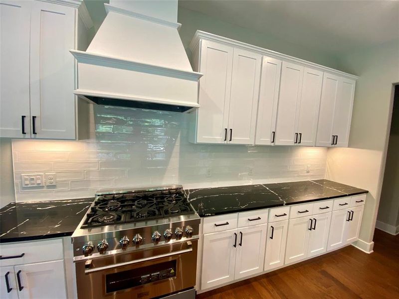 Kitchen with dark hardwood / wood-style floors, premium range hood, white cabinets, and stainless steel stove