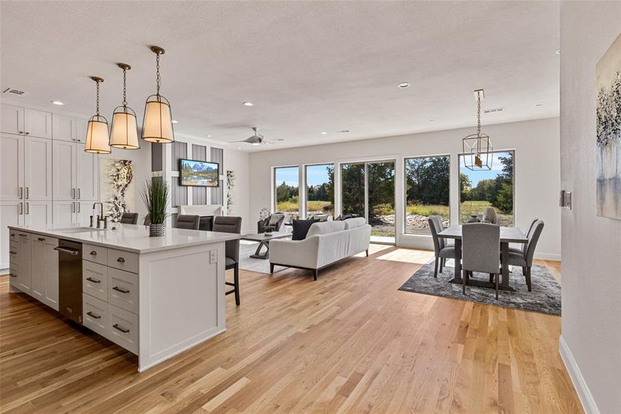 Kitchen featuring an island with sink, ceiling fan with notable chandelier, a kitchen bar, decorative light fixtures, and light hardwood / wood-style floors