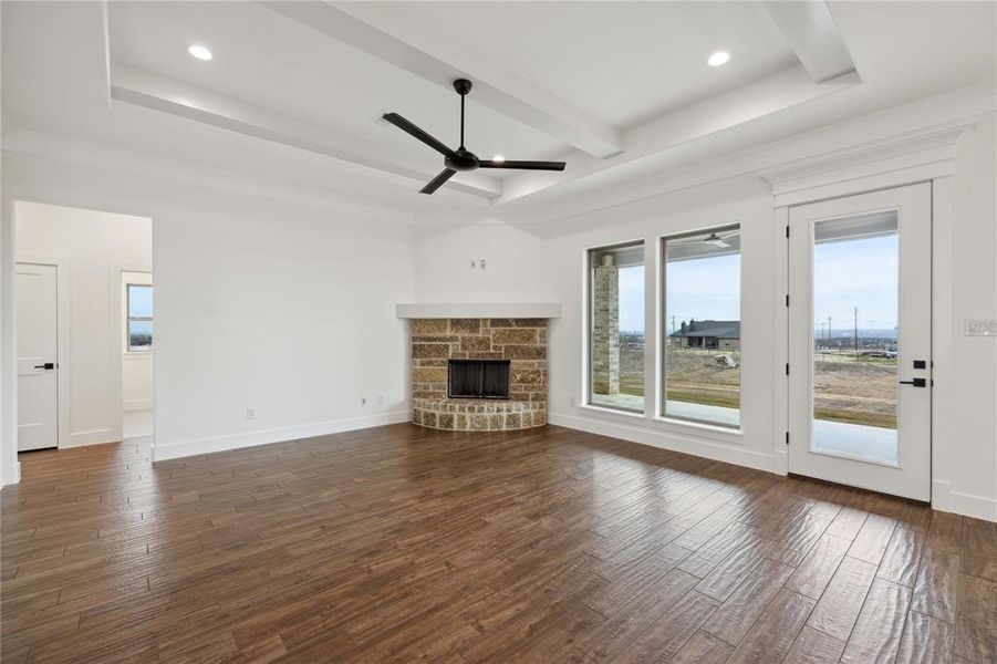 Unfurnished living room featuring dark wood-type flooring, ceiling fan, and a stone fireplace