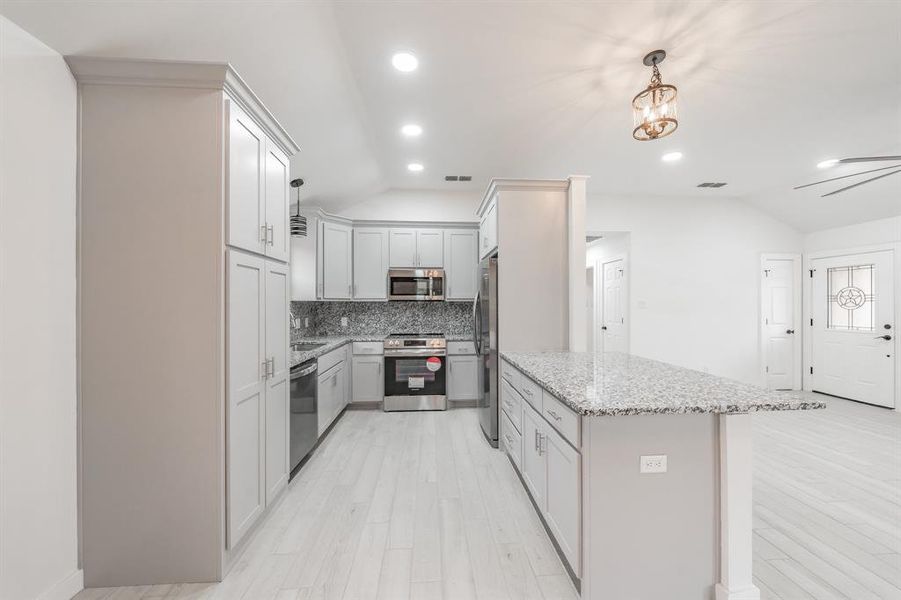 Kitchen with light stone counters, lofted ceiling, decorative light fixtures, light hardwood / wood-style flooring, and appliances with stainless steel finishes