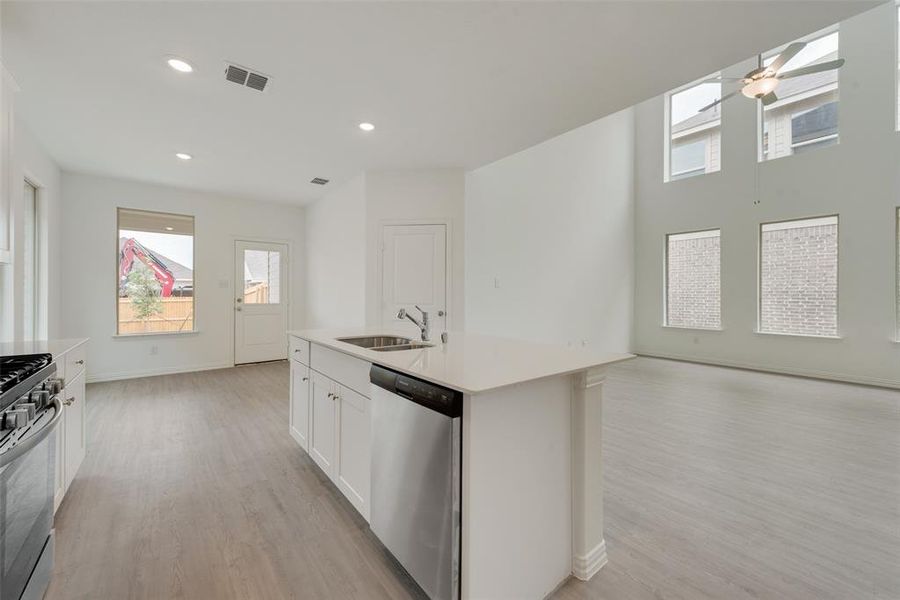 Kitchen with a skylight, sink, a center island with sink, white cabinets, and appliances with stainless steel finishes