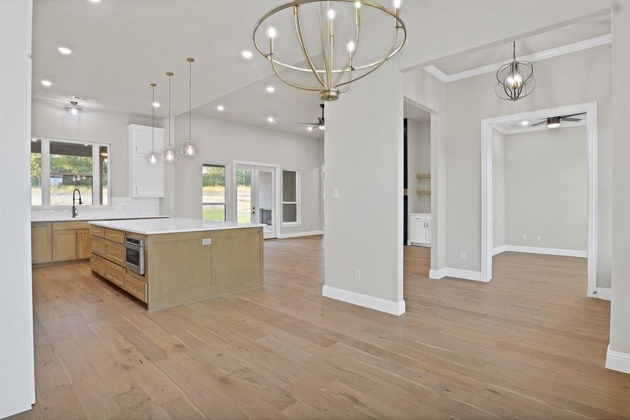 Kitchen featuring sink, light hardwood / wood-style floors, crown molding, a large island, and decorative light fixtures