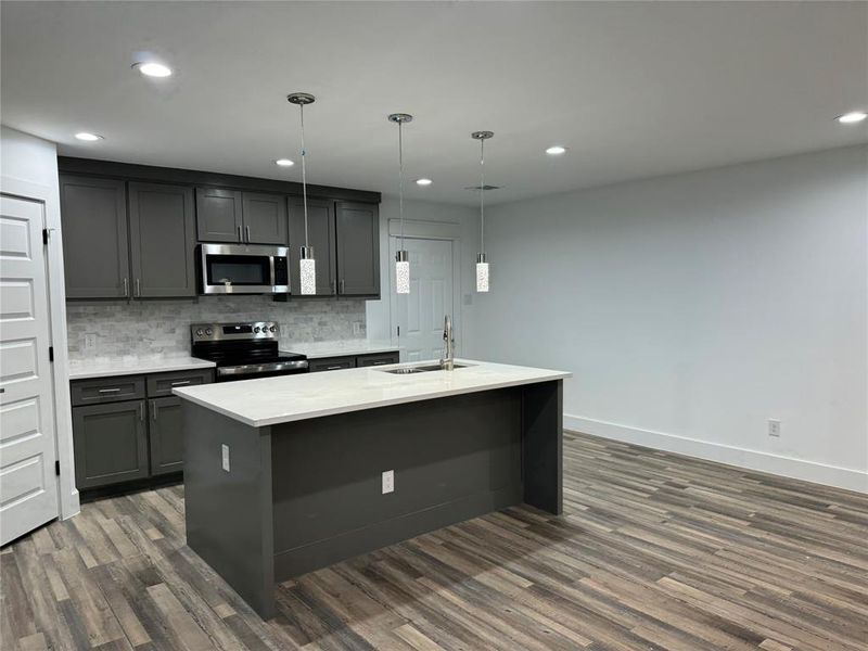 Kitchen featuring appliances with stainless steel finishes, dark hardwood / wood-style floors, pendant lighting, and sink