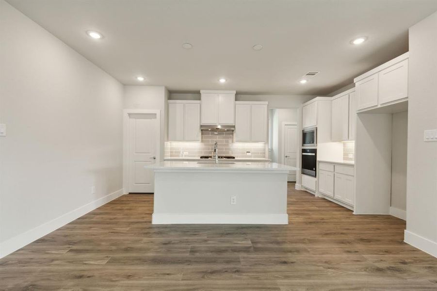 Kitchen with a kitchen island with sink, appliances with stainless steel finishes, hardwood / wood-style floors, and white cabinets