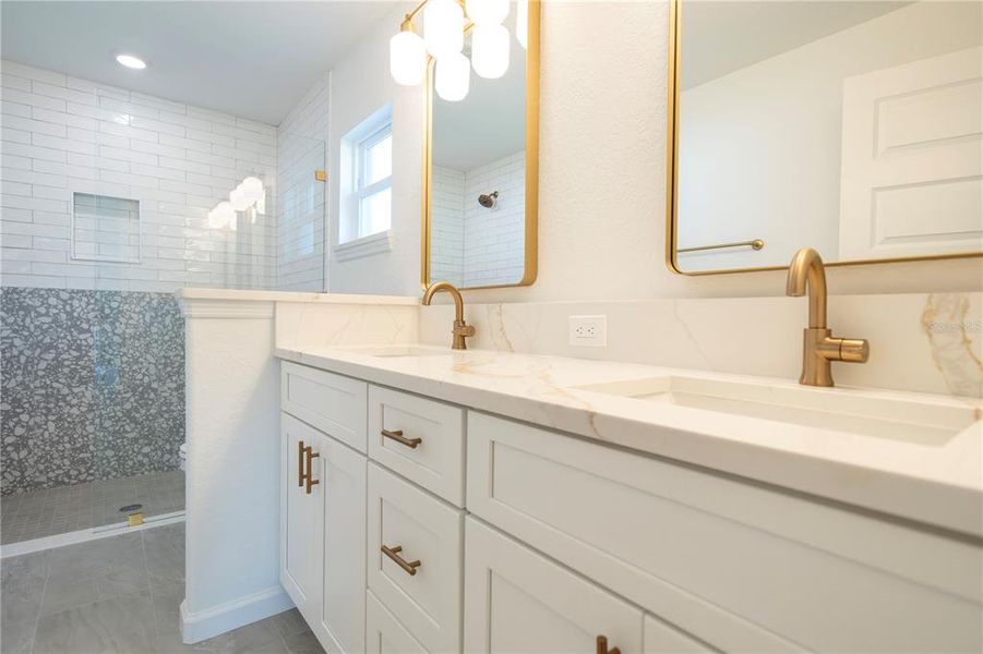 Double sinks in primary bathroom with the same gold toned quartz countertops and gold plumbing fixtures.