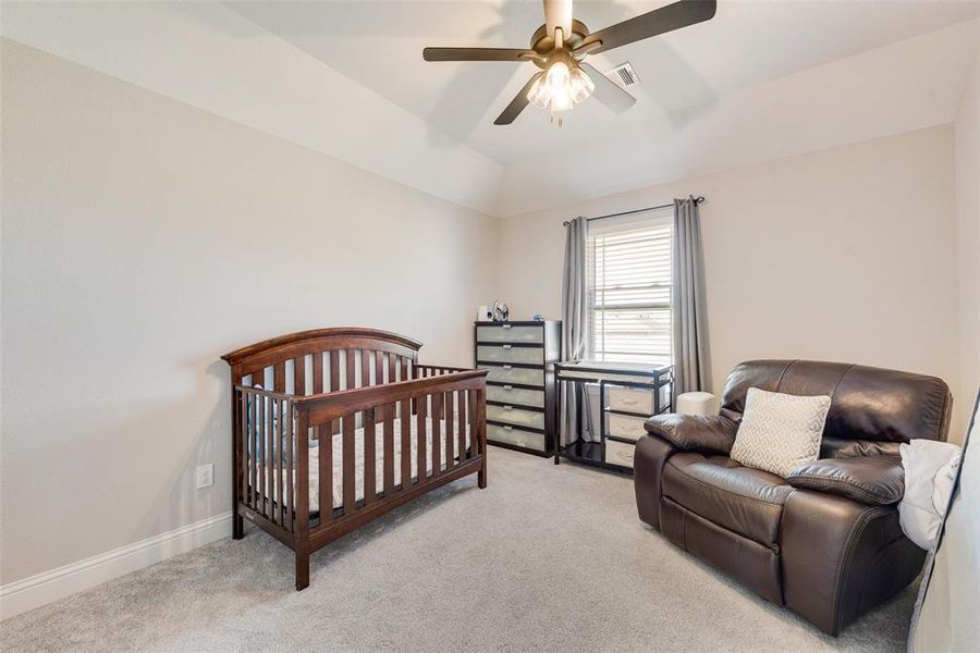 Carpeted bedroom featuring a crib, vaulted ceiling, and ceiling fan