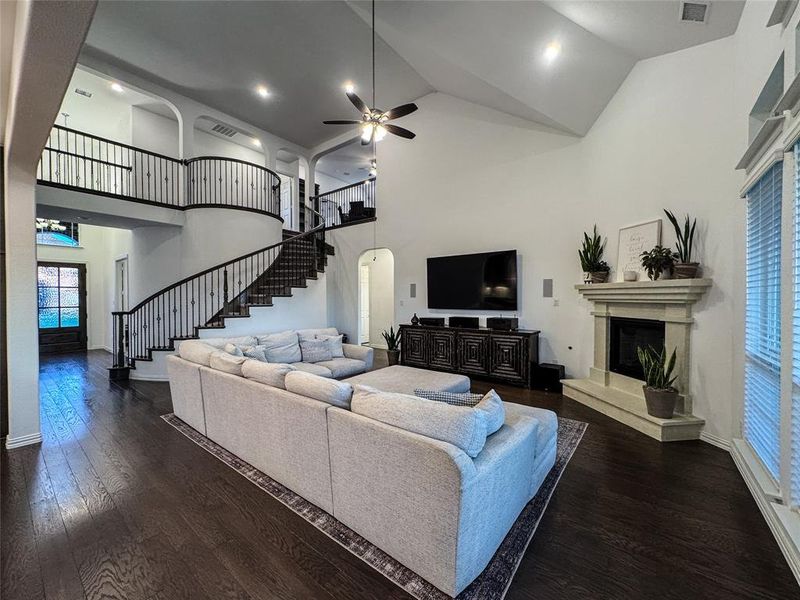 Living room featuring high vaulted ceiling, wood-type flooring, a fireplace, and ceiling fan