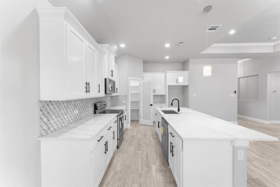 Kitchen featuring light stone counters, sink, an island with sink, white cabinets, and appliances with stainless steel finishes