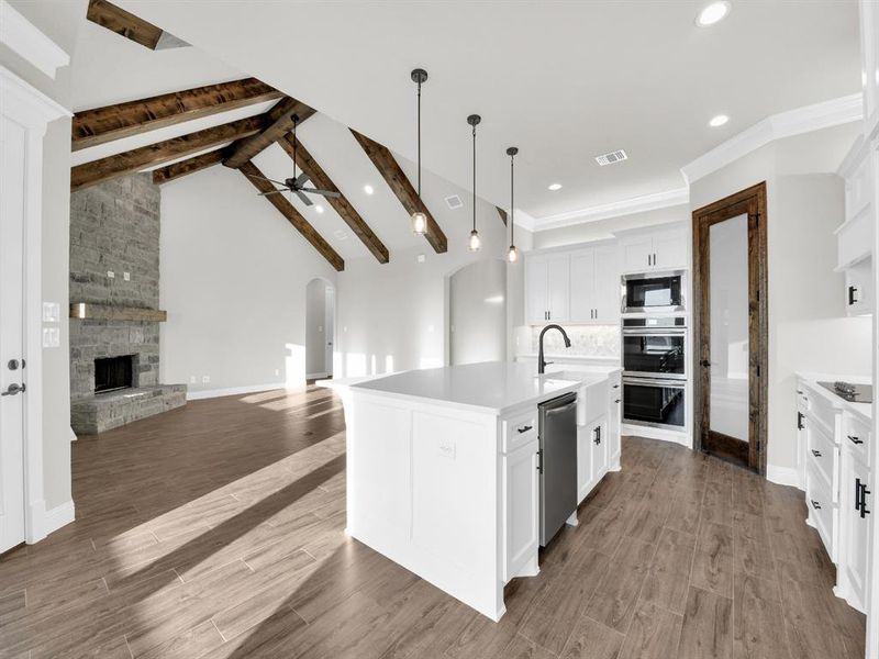 Kitchen with a kitchen island with sink, hardwood / wood-style floors, a stone fireplace, appliances with stainless steel finishes, and pendant lighting