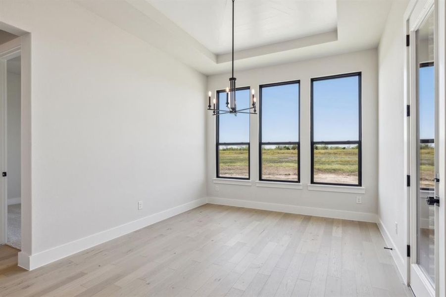 Unfurnished dining area with a tray ceiling, a chandelier, and light wood-type flooring