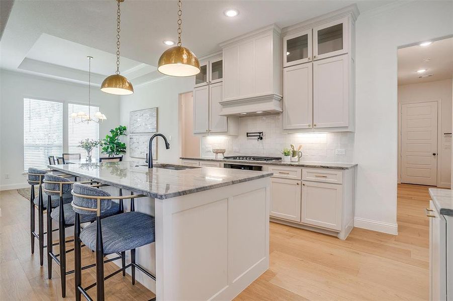 Kitchen featuring custom range hood, tasteful backsplash, white cabinets, light hardwood / wood-style floors, and a raised ceiling
