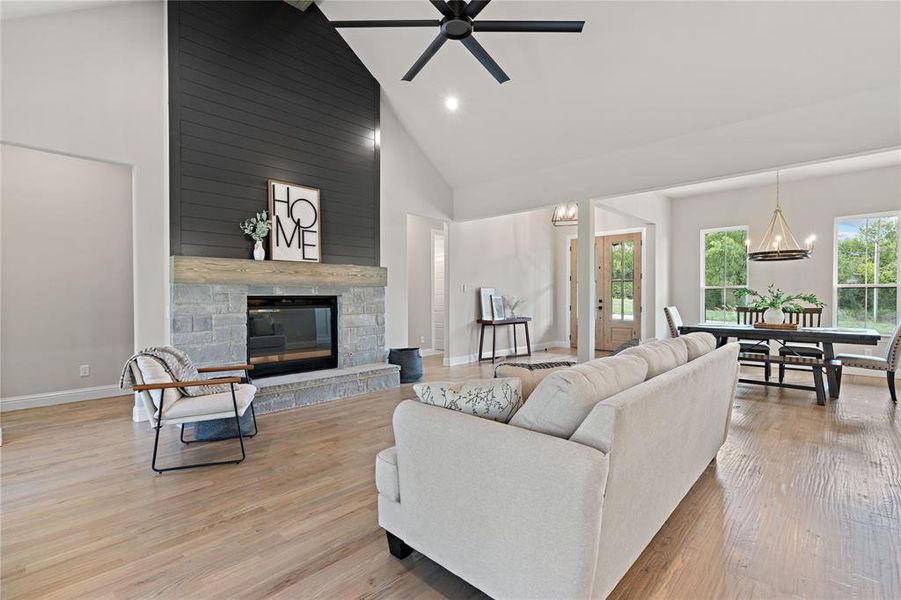 Living room featuring ceiling fan with notable chandelier, light hardwood / wood-style floors, high vaulted ceiling, and a fireplace