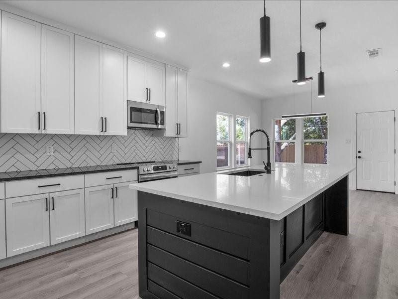 Kitchen with white cabinetry, pendant lighting, an island with sink, appliances with stainless steel finishes, and light hardwood / wood-style flooring