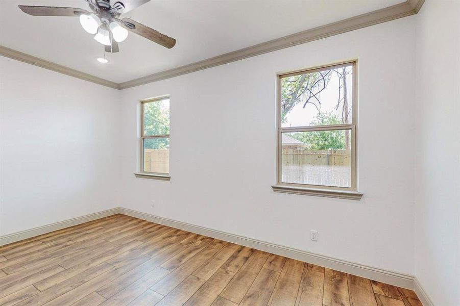 Empty room featuring a healthy amount of sunlight, crown molding, wood-type flooring, and ceiling fan
