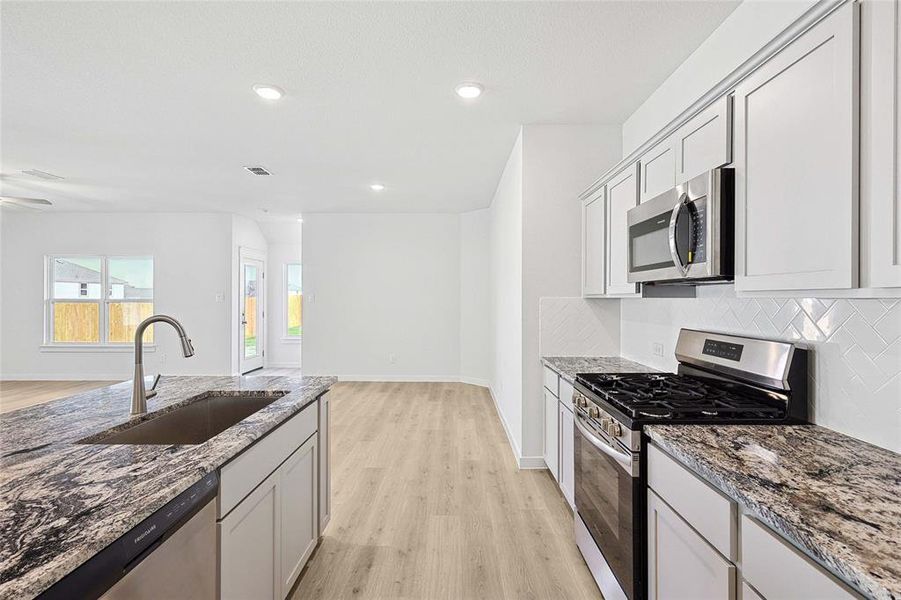 Kitchen with sink, stone counters, appliances with stainless steel finishes, light hardwood / wood-style flooring, and decorative backsplash