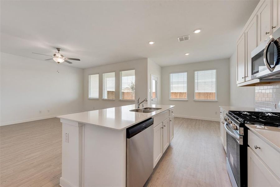 Kitchen with sink, light wood-type flooring, white cabinetry, stainless steel appliances, and a kitchen island with sink