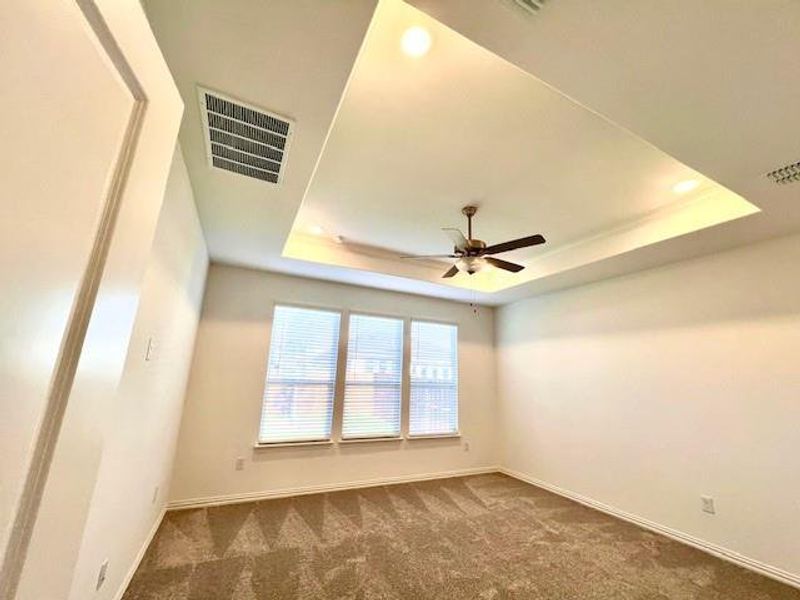 Carpeted empty room featuring ceiling fan and a raised ceiling