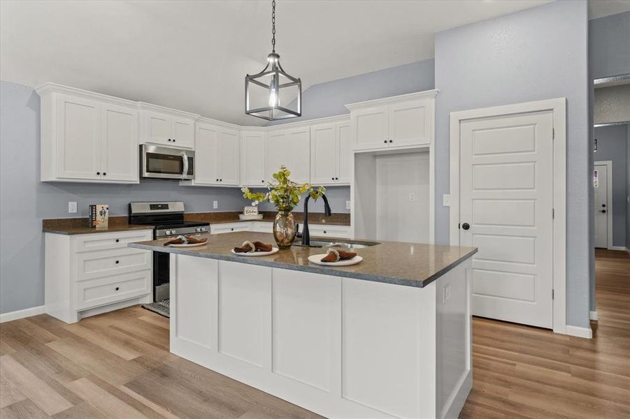 Kitchen featuring light hardwood / wood-style flooring, a center island with sink, sink, white cabinets, and appliances with stainless steel finishes