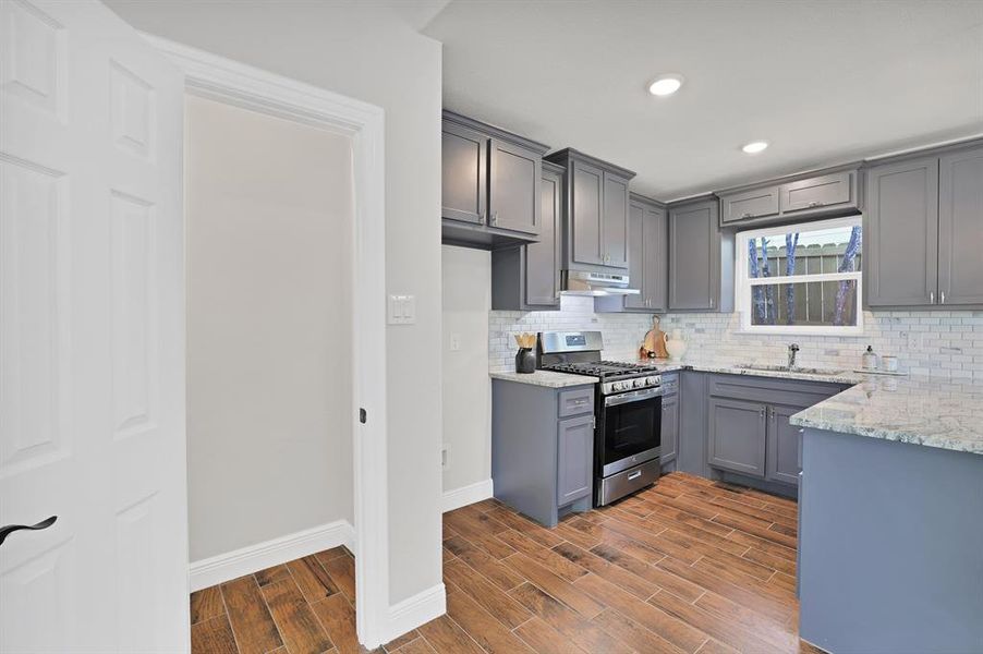 Kitchen with sink, dark wood-type flooring, gray cabinetry, and gas range