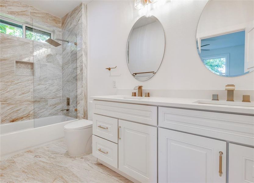 Full bathroom with dual vanity, tile floors, toilet, and tiled shower / bath combo