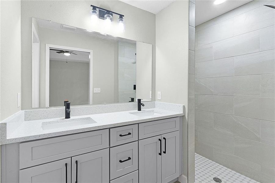Primary bathroom with double vanities, quartz countertop, and tiled walk-in shower