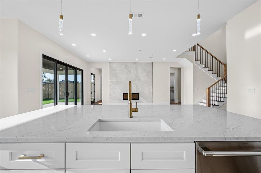 Kitchen featuring light stone countertops, hanging light fixtures, sink, and white cabinetry