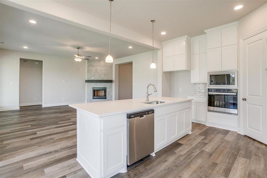 Kitchen featuring a kitchen island with sink, a fireplace, appliances with stainless steel finishes, and light hardwood / wood-style floors